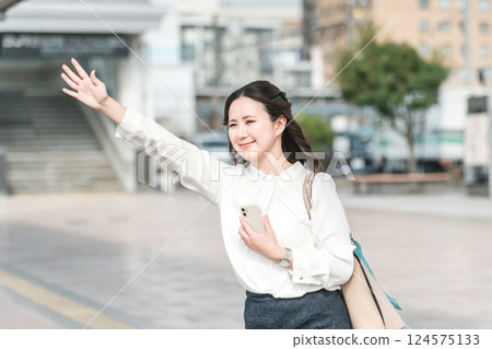 A young Asian business woman raises her hand to hail a taxi at the taxi stand (business trip/transfer) A young Asian business woman raises her hand to hail a taxi at the taxi stand (business trip/transfer) 124575133