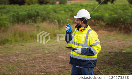 man in a yellow and blue safety vest is standing in a field man in a yellow and blue safety vest is standing in a field 124575288