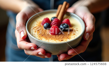 Delicious berry dessert served in a bowl with cinnamon sticks on top and a creamy texture, held by hands 124575608