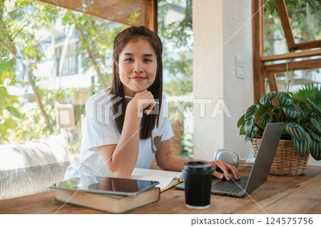 A young woman sits at a wooden desk with a laptop, surrounded by plants, enjoying a bright and airy home office environment. A young woman sits at a wooden desk with a laptop, surrounded by plants, enjoying a bright and airy home office environment. 124575756