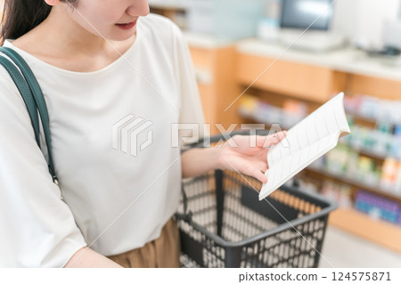 一位女士在藥房、藥店或便利店一邊看著筆記本一邊購買化妝品 124575871