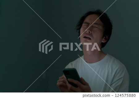 A man operating a smartphone in a dark room 124575880