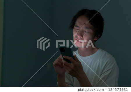 一名男子在黑暗的房間裡操作智慧型手機 一名男子在黑暗的房間裡操作智慧型手機 124575881