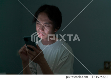 一名男子在黑暗的房間裡操作智慧型手機 一名男子在黑暗的房間裡操作智慧型手機 124575882