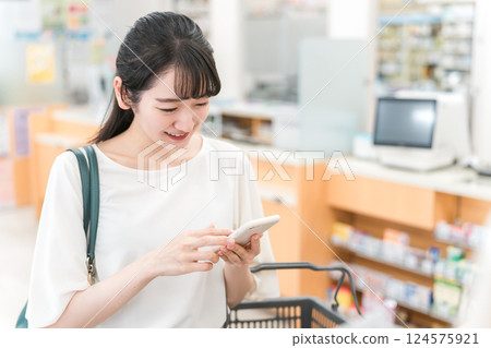 一位女士在藥房/藥店/便利店一邊查看智能手機一邊購買化妝品 124575921
