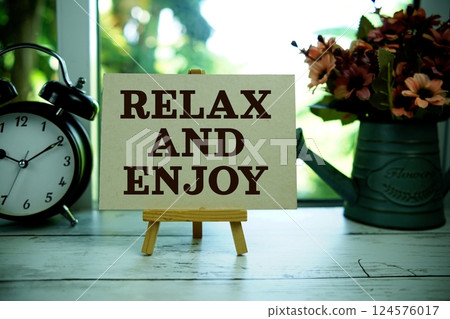 Relax and Enjoy text motivational and inspiration quote with alarm clock on wooden background Relax and Enjoy text motivational and inspiration quote with alarm clock on wooden background 124576017