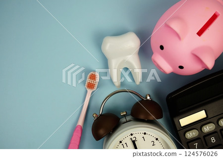 Dental Treatment Costs with toothbrush, calculator, piggy bank and white tooth model top view on blue background Dental Treatment Costs with toothbrush, calculator, piggy bank and white tooth model top view on blue background 124576026