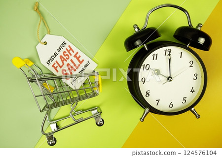 Flash Sale text on price tag with trolley shopping cart and alarm clcok top view on green geometric background 124576104