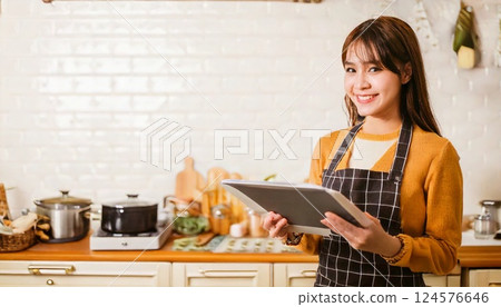 A smiling Japanese woman cooking while holding a tablet in one hand 124576646