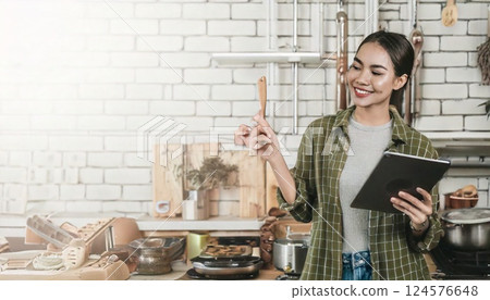 一位微笑的日本女士一手拿著平板電腦，一手做飯 124576648