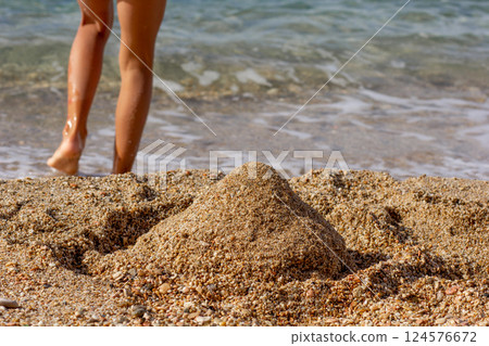 Sand castle on sea beach and child legs Sand castle on sea beach and child legs 124576672