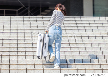 女人提著沉重的行李箱上樓梯 女人提著沉重的行李箱上樓梯 124576753