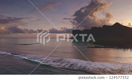 Aerial drone footage captures the beauty of Bora Bora at sunset, with mount Otemanu reflecting on the calm ocean water as gentle waves break along the shore Aerial drone footage captures the beauty of Bora Bora at sunset, with mount Otemanu reflecting on the calm ocean water as gentle waves break along the shore 124577352