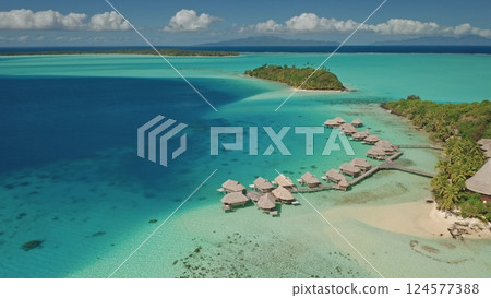 Aerial panorama of luxurious overwater bungalows nestled in pristine turquoise lagoon surrounding tropical island paradise in French Polynesia. Exotic travel romantic vacation getaway. Drone flight 124577388