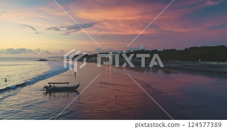 Tourists are enjoying the low tide and colorful sunset on Dreamland Beach, Bali, Indonesia, while a traditional Balinese boat, called jukung, is resting on the shore 124577389