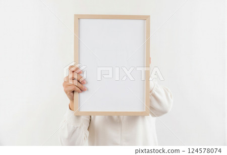 Person gripping top of minimalistic white empty picture frame, vertical orientation, blank isolated backdrop, customization, display poster, creative branding, promotional material, design content 124578074
