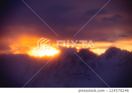 Stunning sunset paints sky with vibrant hues of red, orange, and pink, blending into deep blues and purples. Silhouetted hills create contrast against fiery horizon, adding drama to serene landscape 124578246