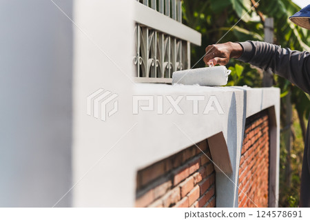Man painting a wall outside with roller for house decoration. 124578691