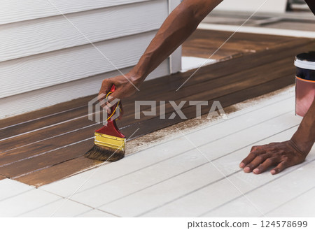 Worker painting decking floor with paint brush. 124578699
