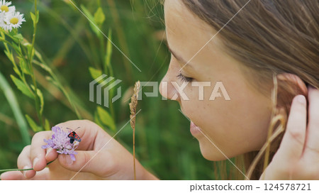 Teenage girl admires a moth on a flower. Warm summer day. Teenage girl admires a moth on a flower. Warm summer day. 124578721
