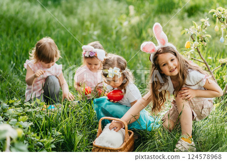 Easter egg hunt. Group Of Children Wearing Bunny Ears Running To Pick Up colorful Egg On Easter Egg Hunt In Garden. Easter tradition. Laughing children in park with basket spring concept 124578968