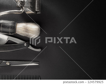 Various barber tools such as clippers, scissors, a comb, and a shaving brush are arranged on a dark surface, illustrating readiness for a grooming session. Various barber tools such as clippers, scissors, a comb, and a shaving brush are arranged on a dark surface, illustrating readiness for a grooming session. 124579925