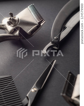 A collection of grooming tools is displayed on a dark background. The tools include scissors, clippers, and a razor, commonly used by barbers for precision cutting. 124579980