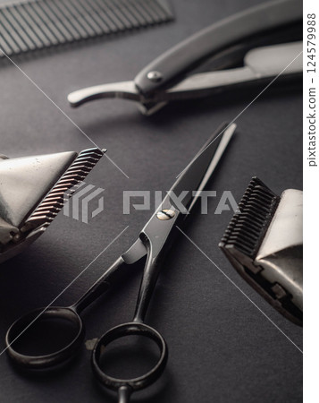 A collection of professional barber tools rests on a dark surface, including scissors, a razor, and combs, highlighting the essential grooming equipment for haircuts. 124579988