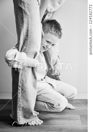 Young happy boy hugging mom's legs. Hyperactive kid holding his mother's legs. Clingy son wanting attention from mommy. Black and white image. 124582772