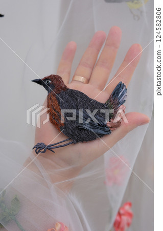 tulle fabric embroidery of flowers and birds on a veil On a thin fabric a woman embroiders straightening beautiful handwork on a mannequin wedding dress with bright decorations tulle fabric embroidery of flowers and birds on a veil On a thin fabric a woman embroiders straightening beautiful handwork on a mannequin wedding dress with bright decorations 124582806