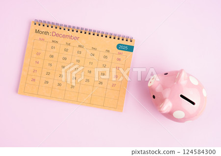 Brown desk calendar for December 2025 and pink piggy bank. 124584300