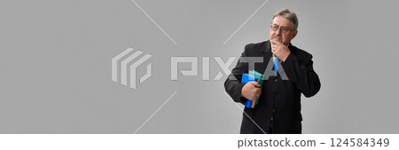 Senior man in suit with hand on chin looking thoughtful while holding books on grey background. Senior man in suit with hand on chin looking thoughtful while holding books on grey background. 124584349