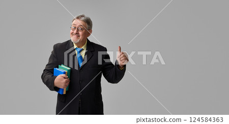 Senior professor in suit holding books and giving confident thumbs up with smirk on grey background. Approval. Senior professor in suit holding books and giving confident thumbs up with smirk on grey background. Approval. 124584363