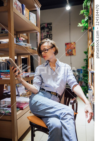 Woman with glasses among shelves with books in university library 124584470