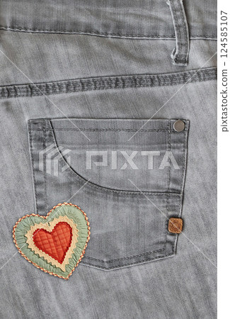 Denim background of gray color with pocket and felt heart. Grey color jeans fabric texture. Vertical background with denim texture, heart-shaped textile patch and pocket. Copy space for text 124585107