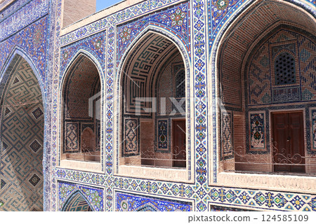Famous landmark - Ulugh Beg Madrasah on Registan square, Samarkand, Uzbekistan. Arches with tile ornament in the courtyard of Ulugh Beg Madrasa. Text on the wall is a quote from the Quran 124585109