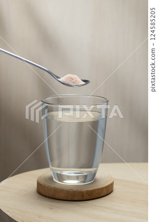 A spoon of Himalayan salt is being added to a glass of drinking water. 124585205