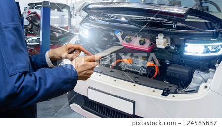 Serviceman with digital tablet next to electric van with open hood. Electric vehicles maintenance. 124585637