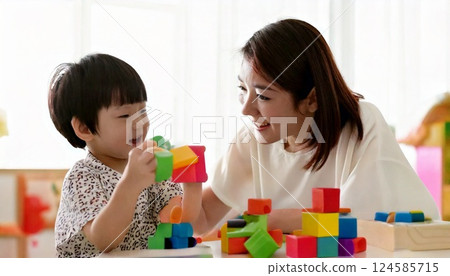 A boy plays with colorful blocks while his kindergarten teacher watches over him 124585715