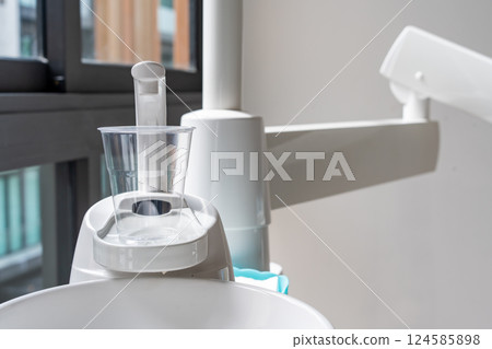 A plastic glass on a cup holder of the modern ceramic mouth cleaning sink in the dentist office near a window, A plastic glass on a cup holder of the modern ceramic mouth cleaning sink in the dentist office near a window, 124585898