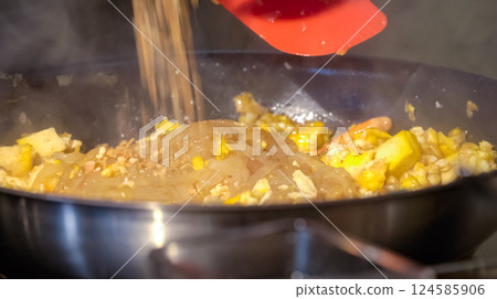 A cook stirs fry Pad Thai noodles in a pan with spatulas on electric stoves. Sauce dishes for cooking traditional Pad Thai. A cook stirs fry Pad Thai noodles in a pan with spatulas on electric stoves. Sauce dishes for cooking traditional Pad Thai. 124585906