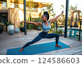 Athletic woman practicing yoga warrior pose on wooden terrace. AI-generated item 124586603