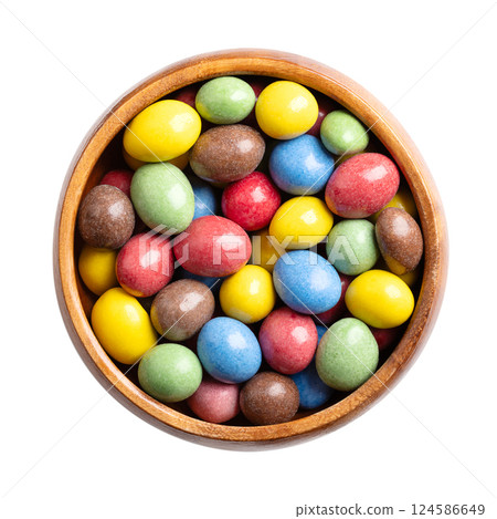 Candy coated milk chocolate peanuts in a wooden bowl. Roasted peanuts, coated with milk chocolate, with multi-colored sugar coating. Colorful sweet and treat. Close-up from above, isolated over white. 124586649