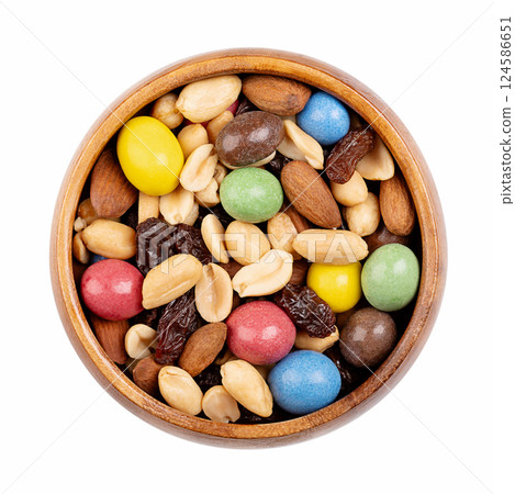 Rainbow trail mix in a wooden bowl. Snack mix of candy coated milk chocolate peanuts, roasted peanuts, raisins, and roasted almonds. Combination of sweets, dried fruits, and nuts. Isolated from above. 124586651