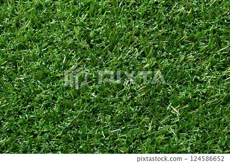 Green artificial turf, plastic grass, surface close up. Green colored surface of synthetic fibers made to look like natural grass. Used in sports arenas, residential lawns and commercial applications. 124586652