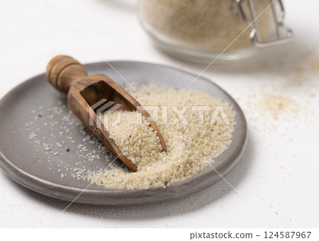 Gray plate of raw uncooked fonio seeds with a wooden scoop on white table closeup. African cereal 124587967