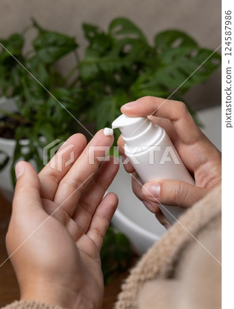 Woman in brown bathrobe applying cream on hand and holding a cosmetic bottle in bathroom 124587986