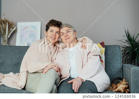 Neutral gender woman hugging her senior mom or grandma and watching TV, sharing tender moment together. Parenting love, care and generations unity concept. Mothers day. Happy family enjoying weekend. 124588036