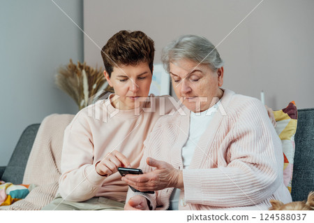 A young woman explaining her senior mother or grandma how to use smartphone. Retired lady discovering mobile technology for calling, texting, buying online, playing games, using medical apps. A young woman explaining her senior mother or grandma how to use smartphone. Retired lady discovering mobile technology for calling, texting, buying online, playing games, using medical apps. 124588037