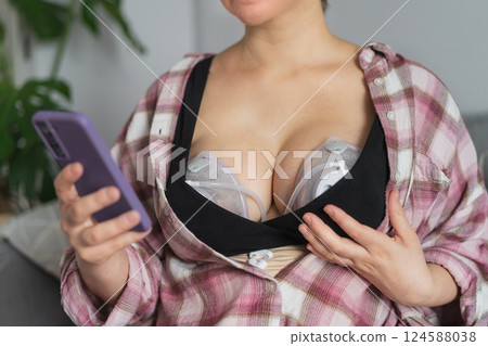 No face woman using electric hands-free breast pump for baby feeding. Woman using breast pump while relaxing at home and checking her phone. Comfortable modern Breastfeeding concept. Selective focus. No face woman using electric hands-free breast pump for baby feeding. Woman using breast pump while relaxing at home and checking her phone. Comfortable modern Breastfeeding concept. Selective focus. 124588038